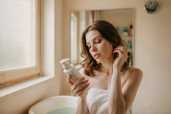 woman reading shampoo ingredient label in bathroom