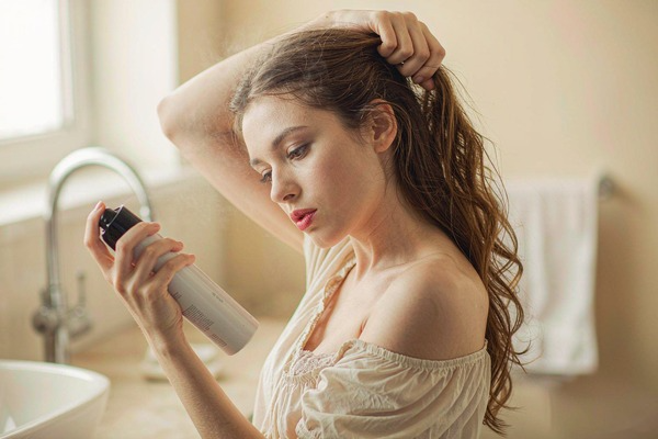 woman spraying dry shampoo into her hair roots